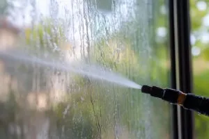 A pressure washer is cleaning a soiled window with water streaks